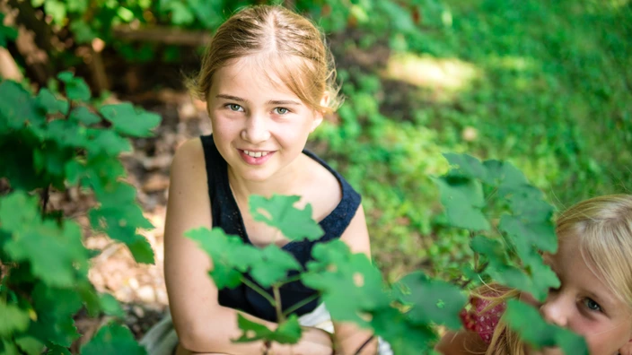 Zwei Kinder knien neben einer Pflanze.