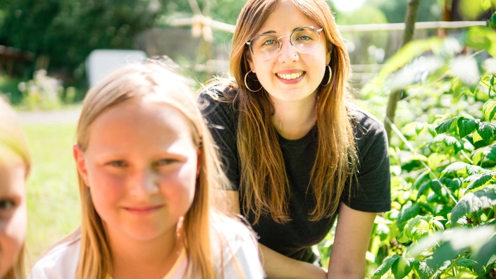 Ein Kind und eine junge Frau knien neben einer Pflanze.