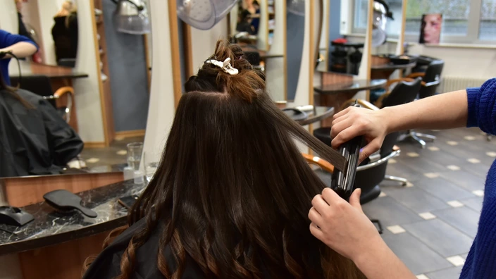 Eine Auszubildende glättet das Haar einer Kundin