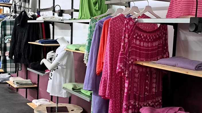 Kleidung hängt an einer Kleiderstange und liegt im Regal