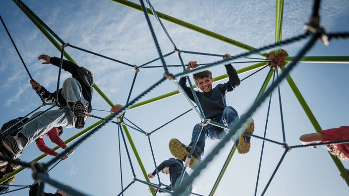 Mehrere Kinder klettern auf einem Netz-Klettergerüst und ein Junge blickt nach unten in die Kamera. Spenden ermöglichen Orte des Spielens für Kinder im CJD.