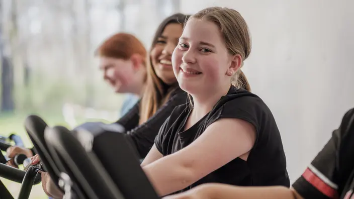 Eine Jugendliche macht Sport auf einem Fitnessgerät. Links und rechts von ihr sind weitere Jugendliche auf Fitnessgeräten zu sehen. Spenden helfen einen Fitnessraum in einer Jugendwohngruppe auszustatten.