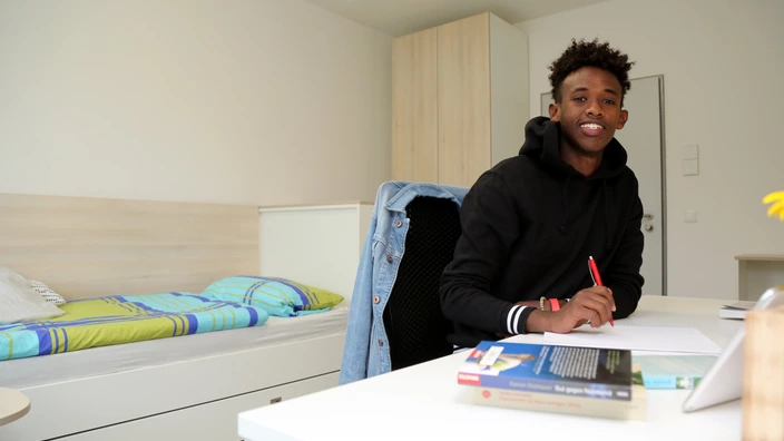 Ein junger Mann sitzt am Schreibtisch in einem Zimmer im Studentenwohnheim Ilmenau.
