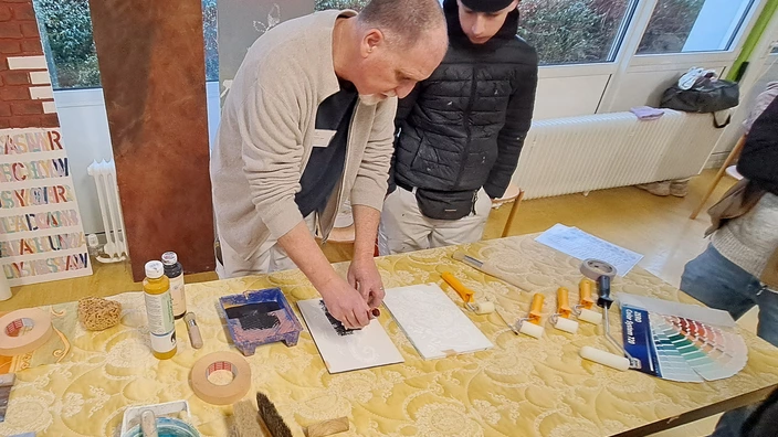 Ausbilder zeigt Schülerinnen und Schüler Techniken zum Malerhandwerk, Auszubildender steht bei Ausbilder