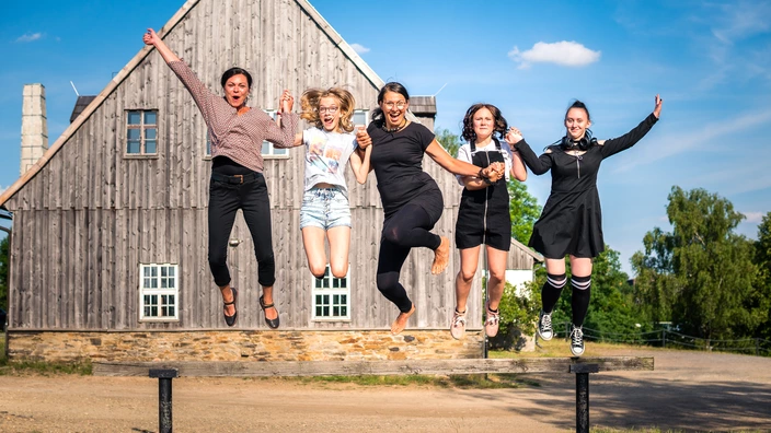 Fünf Personen, die gleichzeitig in die Luft springen und sich an den Händen halten.