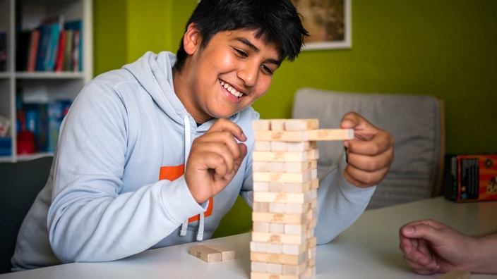 Ein Jugendlicher zieht ein Holzklötzchen aus einem Stapelspiel.