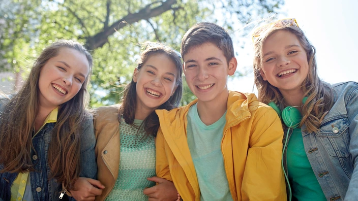  Vier Jugendliche sitzen nebeneinander und lachen.