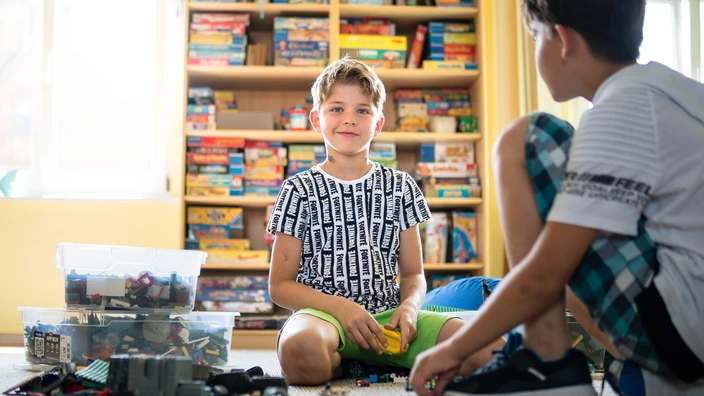 Zwei Kinder sitzen auf dem Teppich und spielen mit Lego.