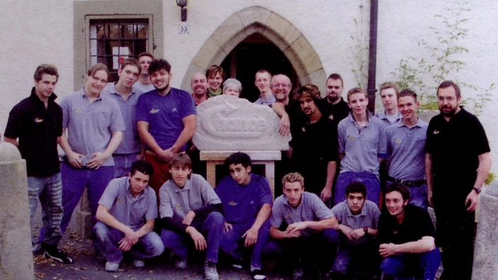 Farbfoto: Eine Gruppe junger Männer und Betreuer steht vor einem historischen Gebäude mit Rundbogenportal. In der Mitte ein Stein mit dem eingemeißelten Wort „Chance“, der offenbar gemeinsam gestaltet wurde. Die Gruppe wirkt stolz und geschlossen – das Bild stammt aus dem Kontext des Projekts Chance im CJD und vermittelt Gemeinschaft und Perspektivarbeit.