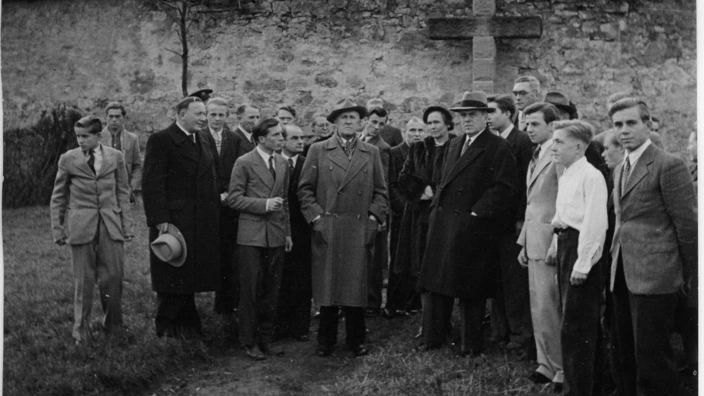 Schwarzweißfoto einer größeren Gruppe von Männern, Frauen und Jugendlichen in formeller Kleidung vor der Burg Kaltenstein. Die Personen stehen im Halbkreis im Vordergrund und scheinen auf eine Führung oder ein Ereignis zu warten. Im Hintergrund ist die historische Burg mit markantem Turm und Natursteinfassade zu sehen. Das Bild vermittelt eine Atmosphäre der Nachkriegszeit.