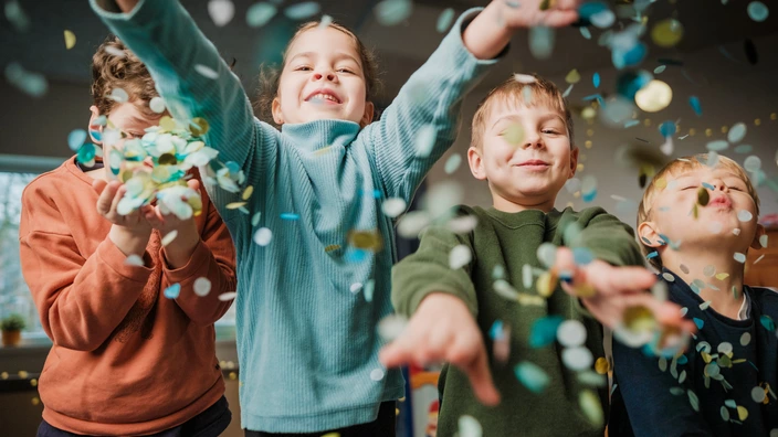 Vier Kinder spielen freudig mit Konfetti, das durch die Luft fliegt