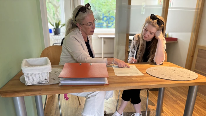 Ronja und Frau Sander sitzen an einem Bürotisch und besprechen ein Dokument