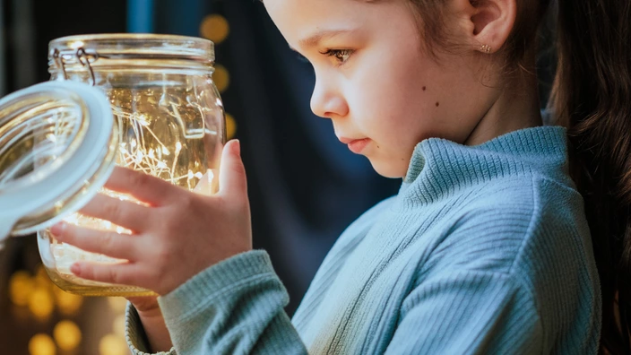 Ein kleines Mädchen schaut in ein Glas mit Lichtern, das sie in der Hand hält. Eine Testamentsspende schenkt Kindern Geborgenheit über das eigene Leben hinaus.