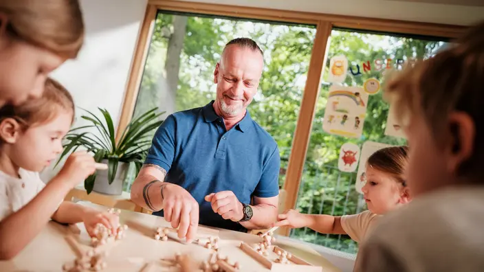 Ein CJD Erzieher spielt ein Holz-Spiel zusammen mit mehreren Kindern einer CJD Kita.