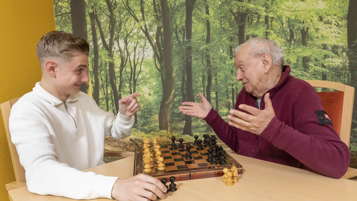 Ein junger Mann spielt an einem ältere Herren Schach.