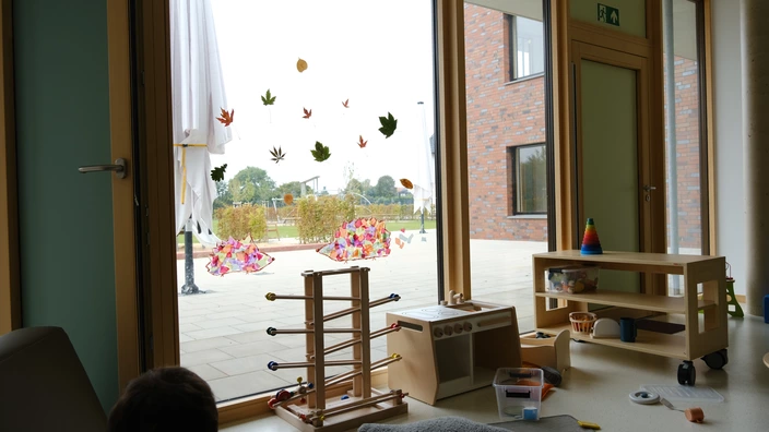 Blick aus einer Kita nach draußen in den Garten, viel Spielzeug liegt rum, auf sind mehrfach beklebt (Mäuse und und Blätter)