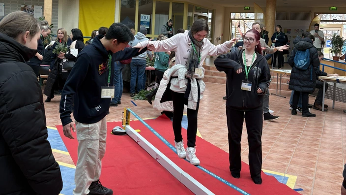 Zwei Teilnehmende stützen eine Teilnehmende beim über die Slackline gehen