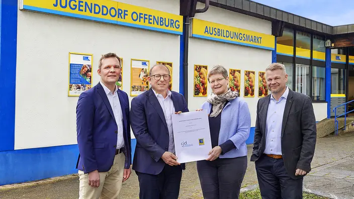 Vier Personen von EDEKA Südwest und CJD vor dem Ausbildungsmarkt bei der Unterzeichnung der Kooperationsvereinbarung.