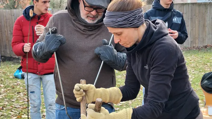 Ein Pädagoge und eine Pädagogin mit Handschuhen und Feuergreifern