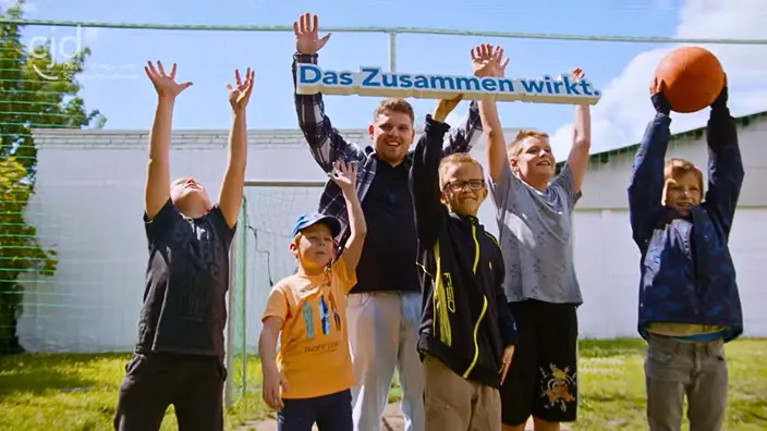 Mehrere Kinder und ein Erzieher des CJD jubeln und halten ein Schild mit dem CJD-Motto Das Zusammen wirkt