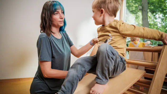 Eine Erzieherin in einer CJD-Kita stützt ein Kind auf einer Rutsche