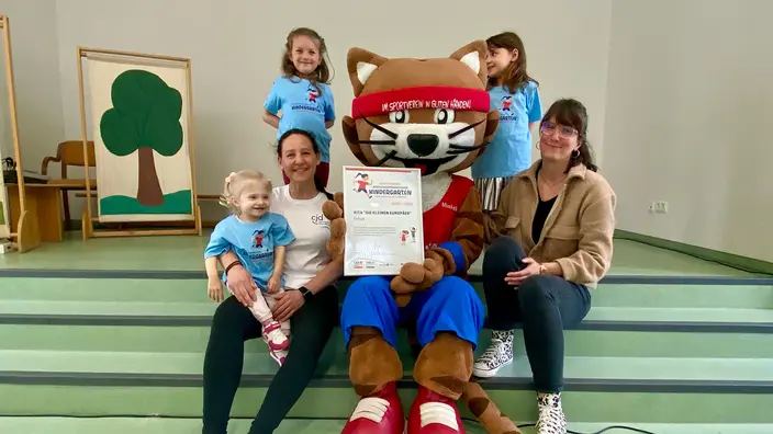 Maskottchen Muskelkater mit zwei Frauen und drei Kindern bei der Zertifikatsübergabe