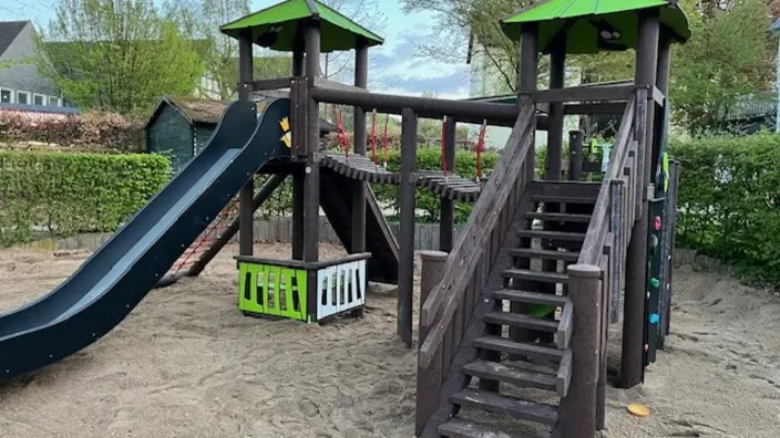 Klettergerüst auf Sand gebaut mit grünem Dach. Rutsche