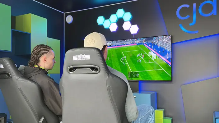 2 Personen sitzen in Gaming-Stühlen vor einem Monitor und spielen FIFA.