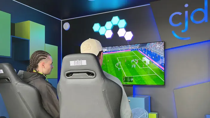 2 Personen sitzen in Gaming-Stühlen vor einem Monitor und spielen FIFA.