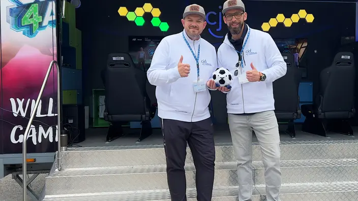 Florian Bogdanow und Martin Nieher stehen vor dem geöffneten Game4All-Anhänger. Sie haben einen Fußball in der Hand.