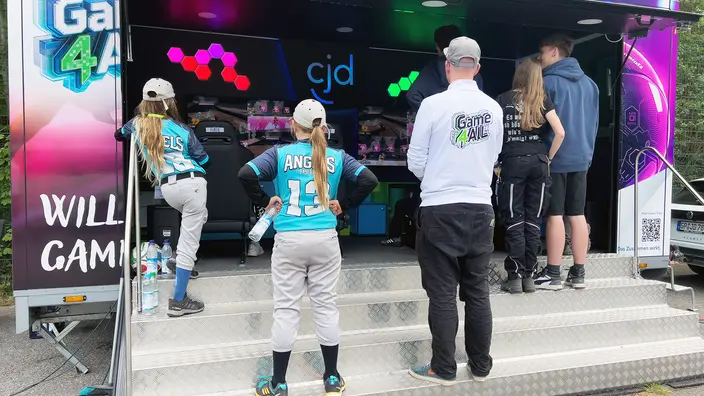 Mehrere Personen stehen vor dem Game4All-Anhänger und schauen den Spielern zu.