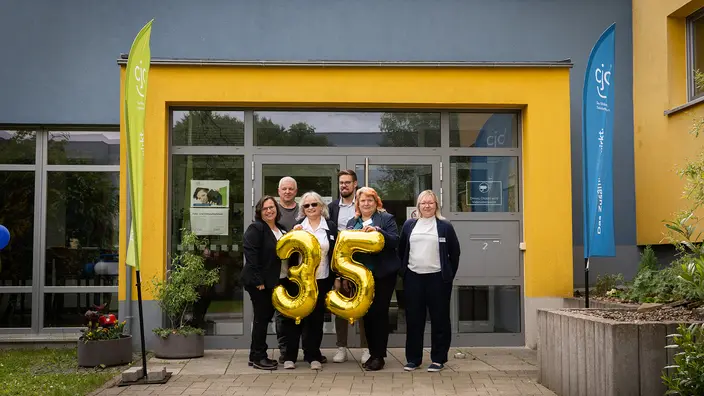 Sechs Personen stehen vor dem Eingang des CJD in Ilmenau. Sie halten große, goldene Folienballons 35.