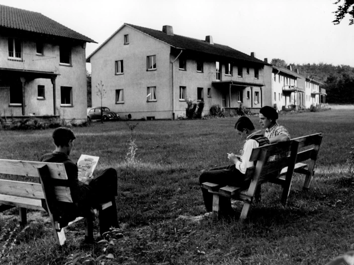 Schwarz-weiß-Foto: Menschen sitzen auf Bänken vor Wohnhäusern, Gemeinschaft und Wohnen im CJD in früheren Jahren.
