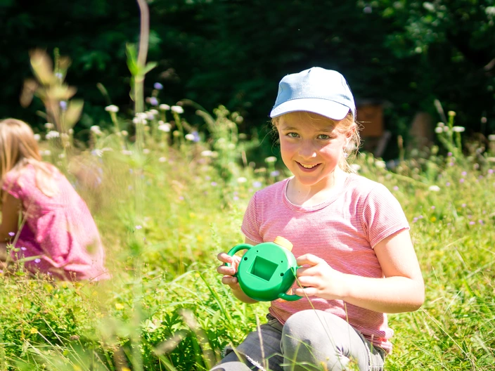 Ein Kind kniet mit einer Becherlupe auf der Wiese.