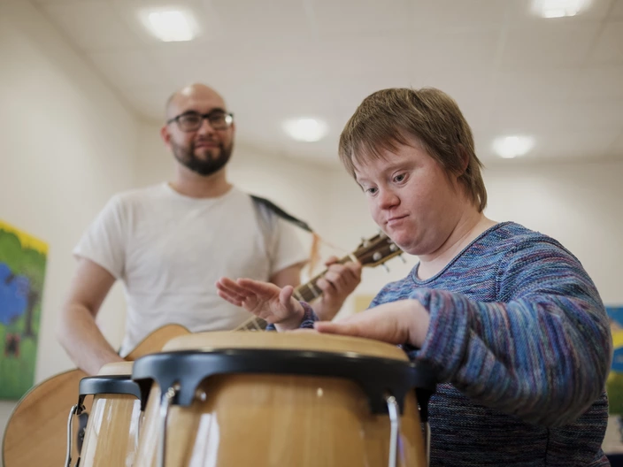 Gemeinsames Musizieren. Ein Pädagoge mit Gitarre und eine Frau mit Trommeln