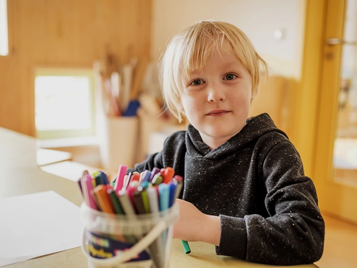 Ein Kind beim Malen mit einer Dose Stifte