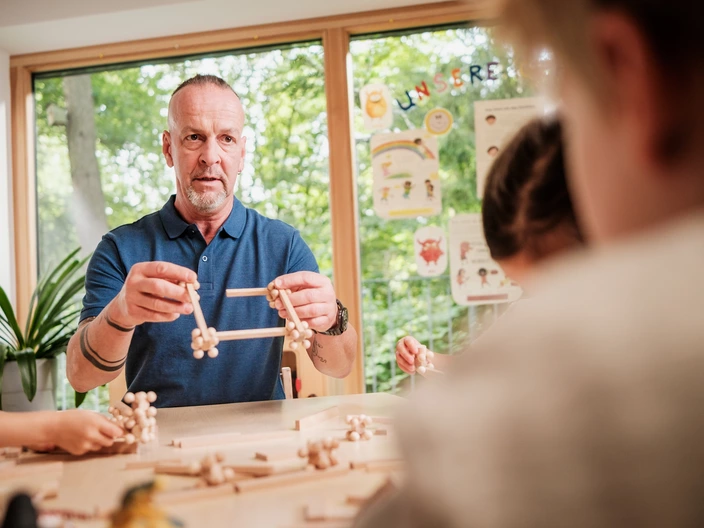 Ein CJD Erzieher zeigt Kindern in einer CJD Kita, was man aus Holz bauen kann.