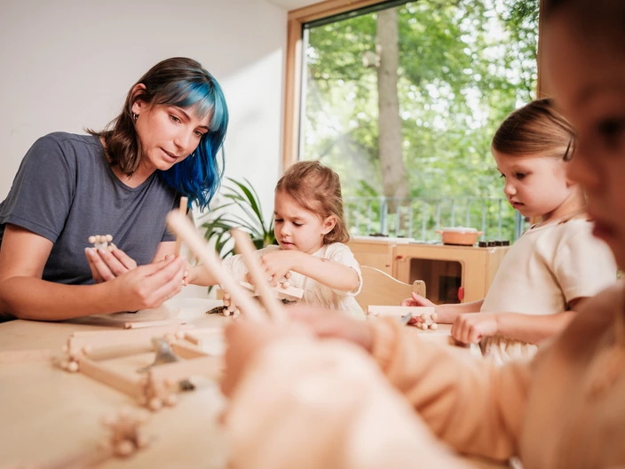 Eine CJD Erzieherin spielt ein Holz-Spiel zusammen mit drei kleinen Mädchen.