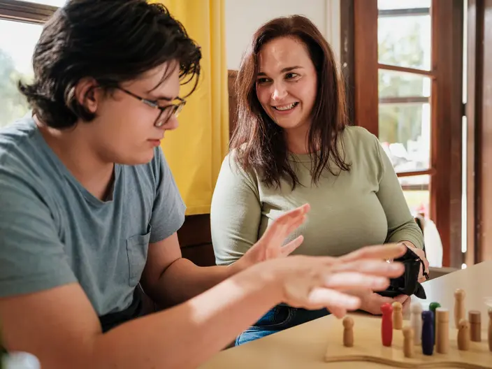 Eine CJD Erzieherin hört einem Jugendlichen zu, der mit Hilfe von Holz-Figuren seine Familienaufstellung nachstellt.